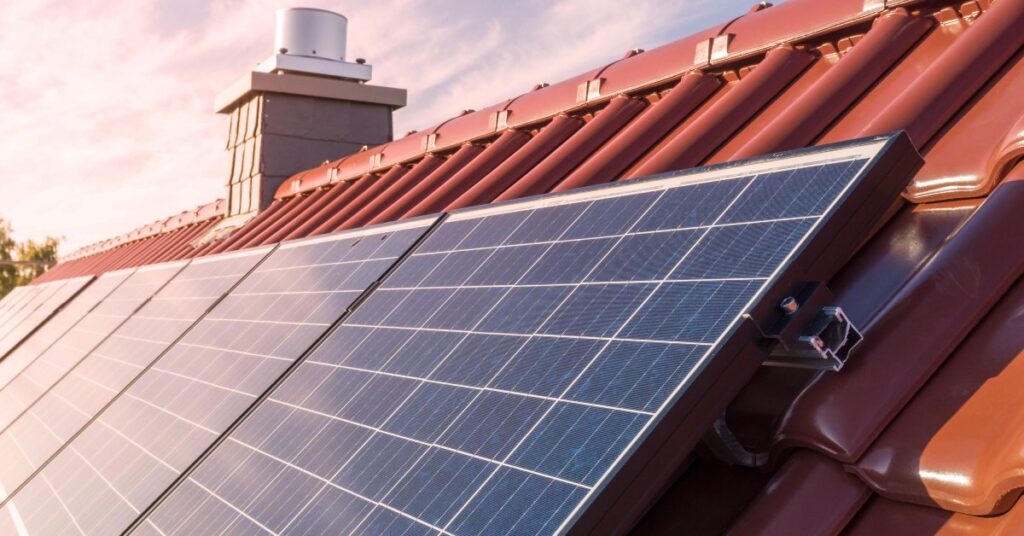 Everything You Need To Know About Solar Panels in 2025 2 Solar panels with multiple cells placed on a roof with metal brown shingles next to a chimney on a sunny day.