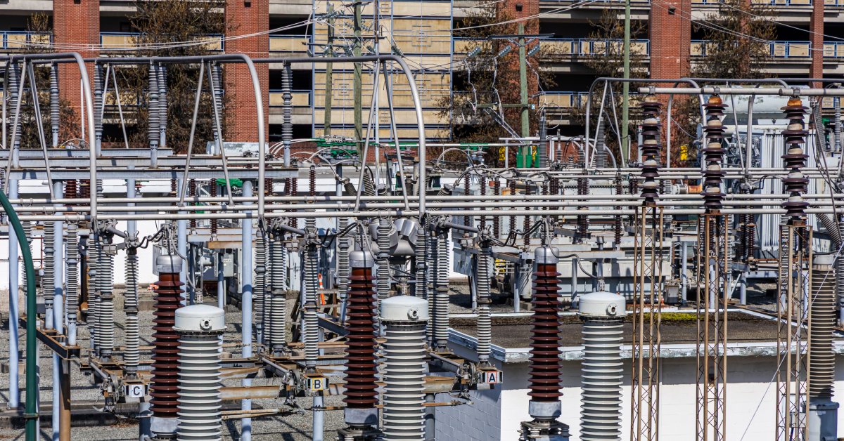 A municipal power grid with multiple wire connections, antennas, coils, cables, and small lights next to a parking garage.