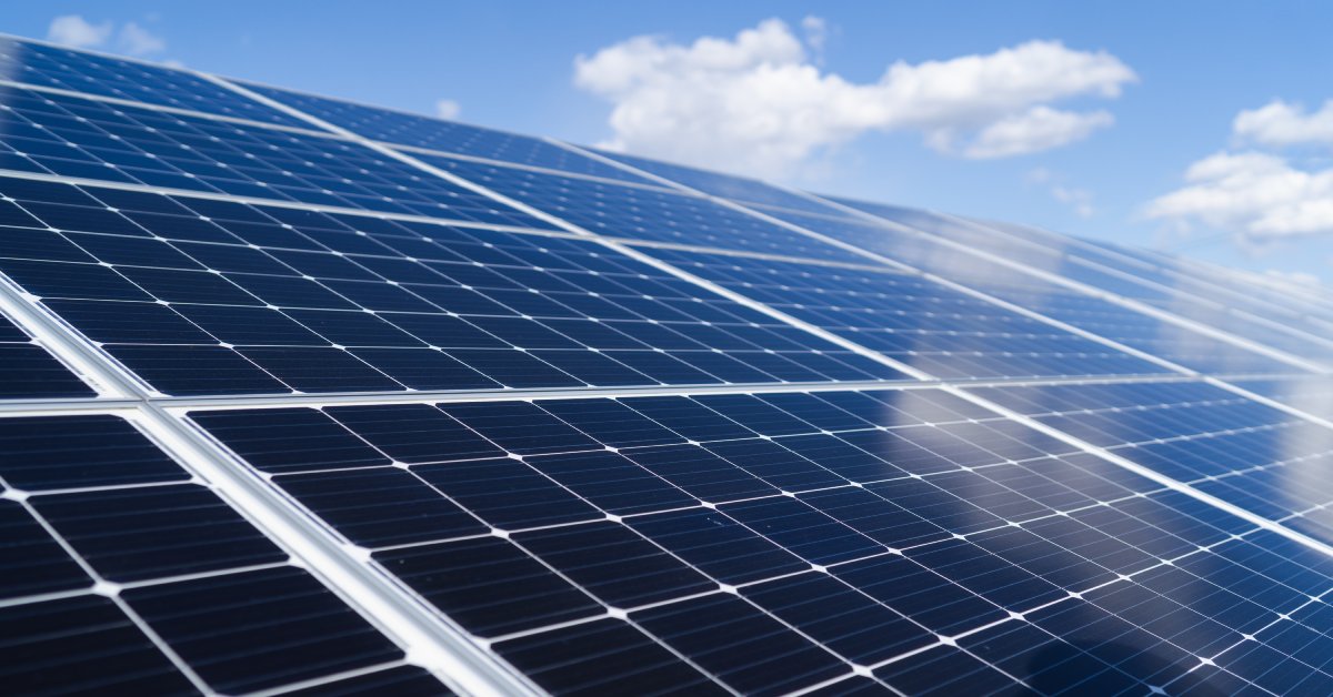 Large interconnected solar panels, placed directly under the sun, reflecting a blue sky with a few clouds.