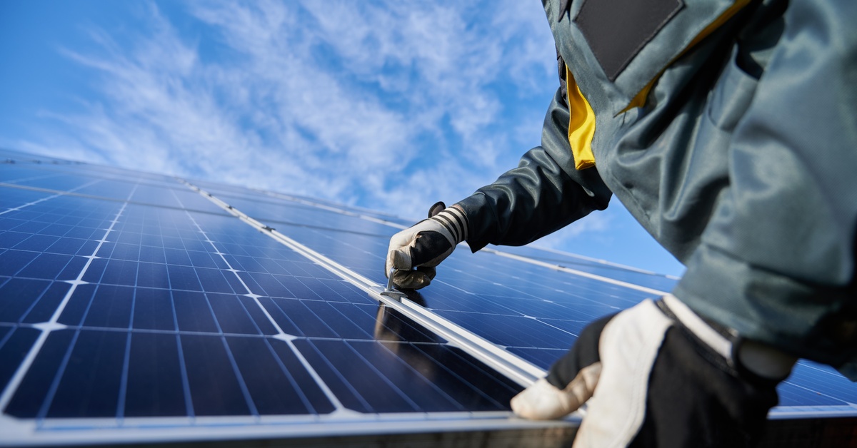 Learn 6 Worker wearing protective gloves and a heavy-duty jacket installing a large solar panel on a sunny day.