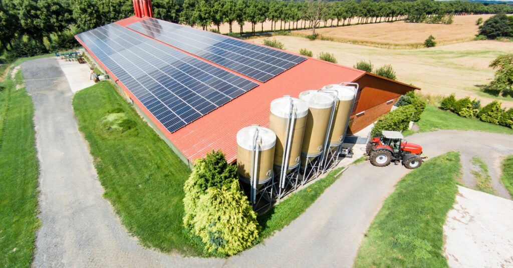 Large barn with multiple rows of solar panels installed on the roof, next to four small towers, and a red truck.
