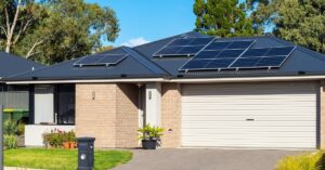 One-story home with a large white garage door, brick walls, and a sloped roof with multiple solar panel units.