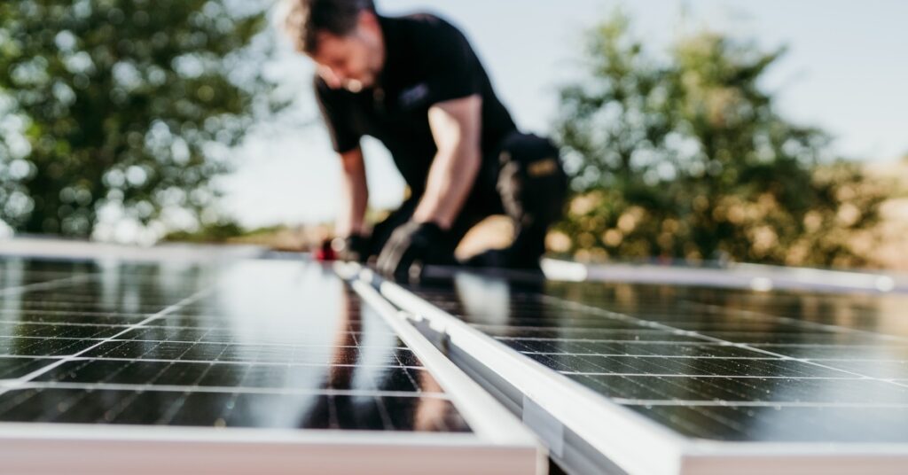 Maintaining Your Residential Solar Power System 2 Blurred man wearing black clothes and protective gloves, touching a solar panel with trees in the background.