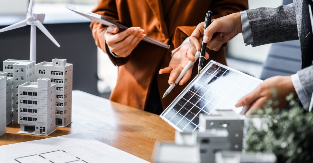 A Guide to Solar Power and LEED Certification 2 Two people holding tablets and discussing while standing behind a desk with building models and solar panels.