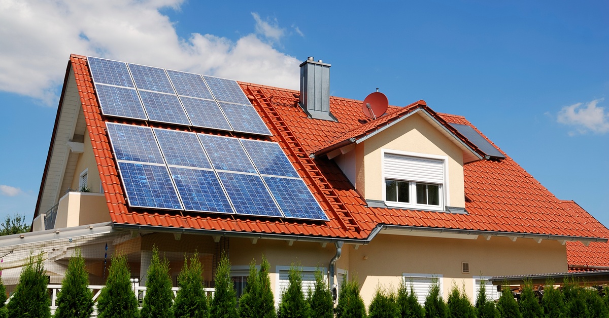 Learn 3 Two-story home with a large angled roof covered in brown shingles with multiple rows of solar panels on the left.