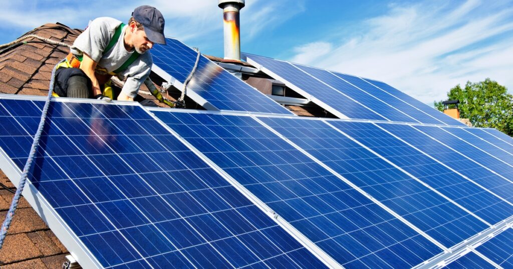 What the Expiration of the Residential ITC Program Means 1 A man wearing a hat holds the edge of a large solar panel on the roof of a house covered in solar panels.