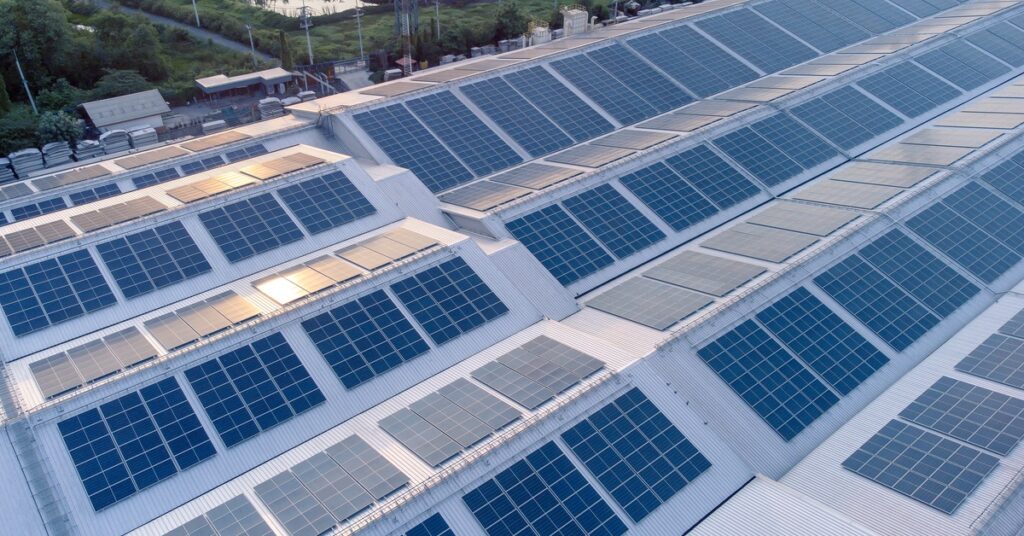 Commercial Solar Power Solutions for Warehouses 1 Rows of solar panels are installed on the roof of a building in a slightly angled position with greenery in the background.