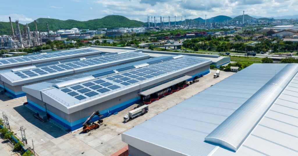 Commercial Solar Power Solutions for Warehouses 3 An aerial view of four large rectangular buildings containing multiple rows of solar panels on their roofs on a sunny day.