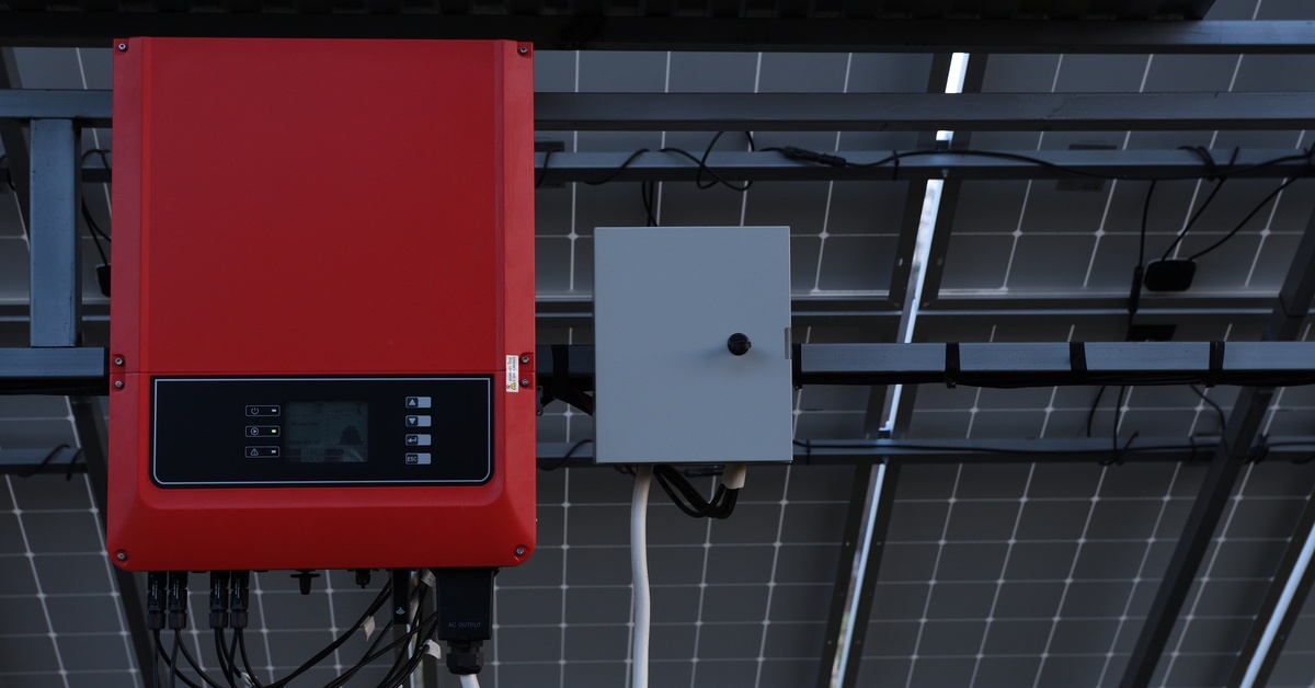 Engineering Behind Modern Solar Power Solutions 2 A red box with a digital panel, multiple buttons, and cables, attached to the back of a large row of solar panels.