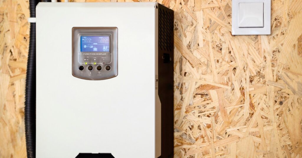 Integrating Tesla Powerwalls With Electrical Systems 2 A solar inverter with multiple cables and a small digital screen, mounted on a brown wall between white door frames.