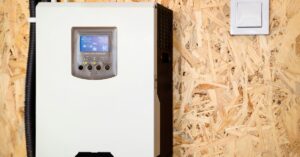 FAQ 7 A solar inverter with multiple cables and a small digital screen, mounted on a brown wall between white door frames.