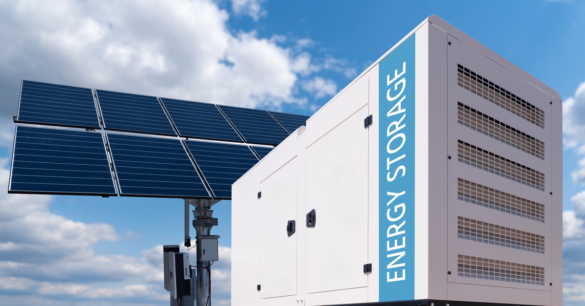 How Tesla Megapack Batteries Stabilize the Electrical Grid 2 A large power battery displaying the words “energy storage,” placed in front of a structure with solar panels.