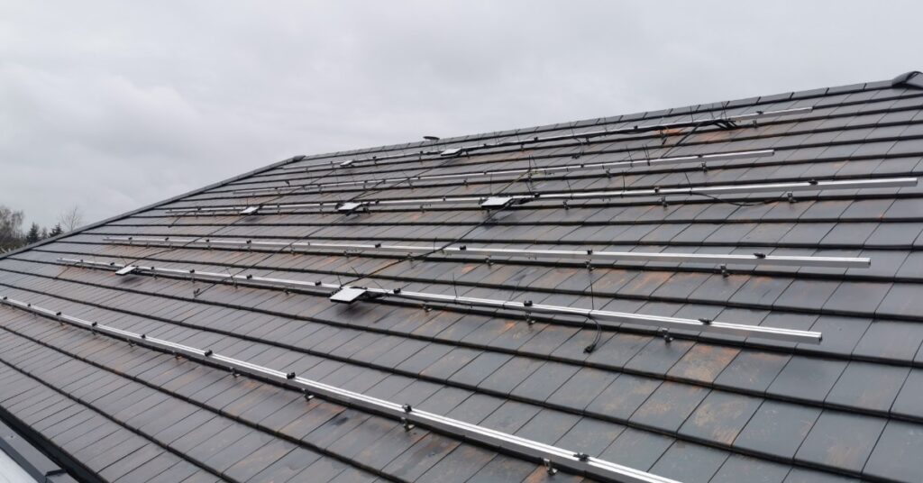 Microinverters vs. String Inverters for Home Solar Power 1 A roof covered in small shingles, with a large metal structure spreading across with small microinverters attached.