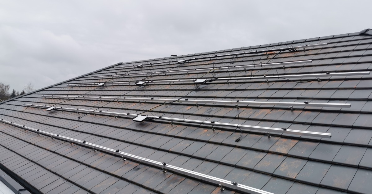 Learn 2 A roof covered in small shingles, with a large metal structure spreading across with small microinverters attached.