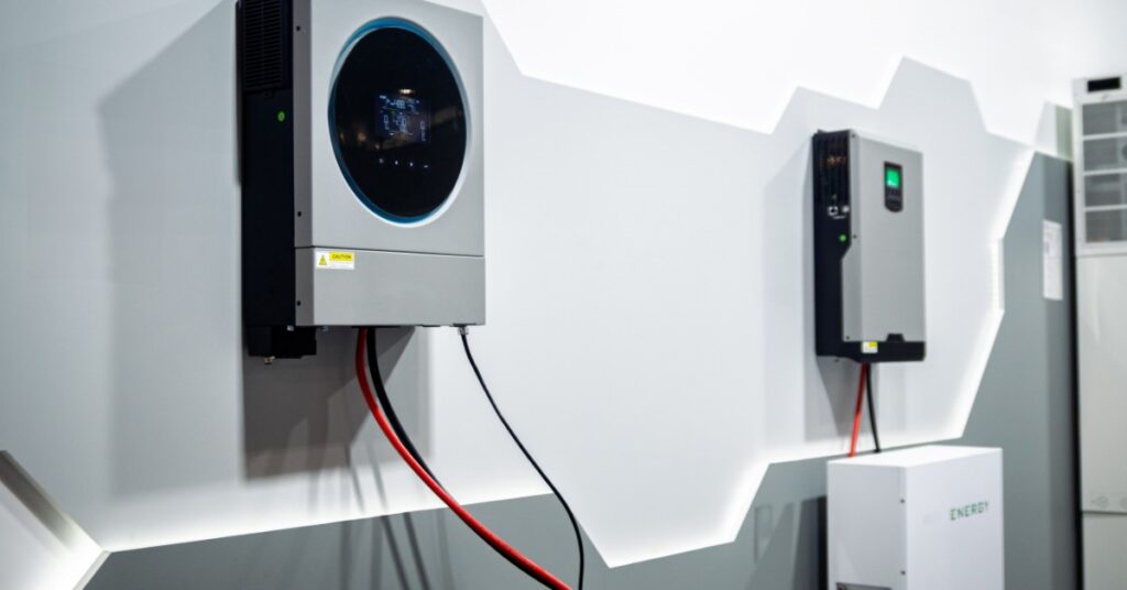 Tesla Solar Powerwall Operating Modes Explained 5 Two small metal power storage units and cables connected at the bottom placed on a white wall with grey stripes.