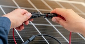 FAQ 7 A close-up of two hands holding a plastic connector with a red cable, over a large solar panel with multiple cells.