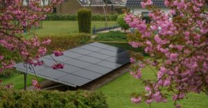 FAQ 6 Three rows of solar panels placed over lush grass, surrounded by bushes and cherry blossom trees, next to a house.