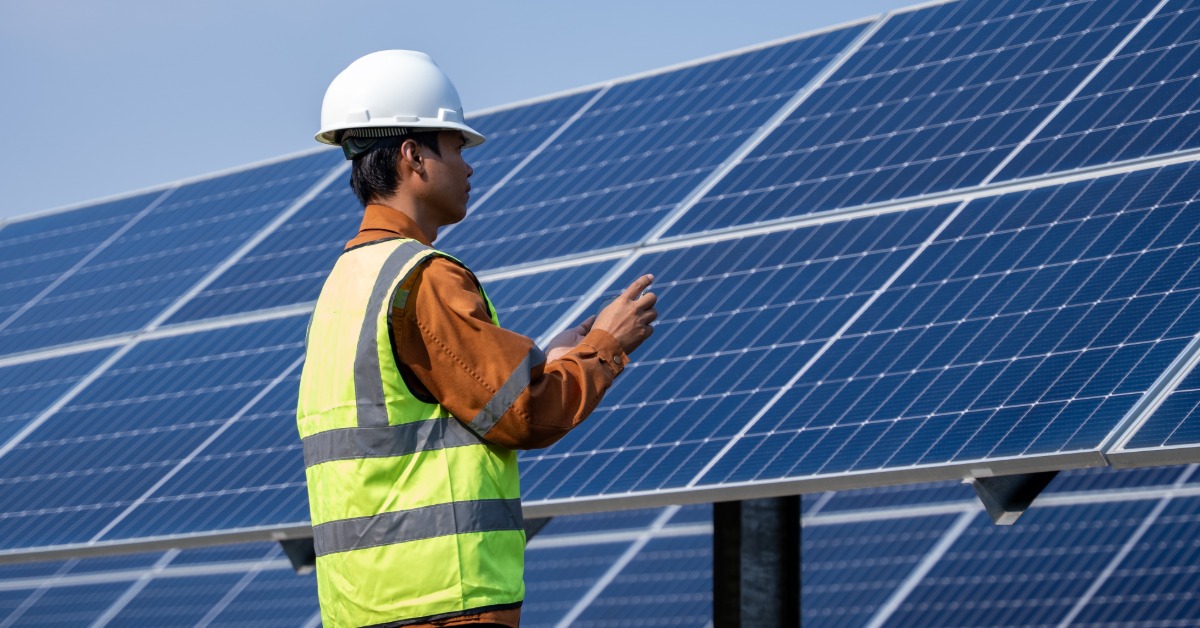 Inverter Efficiency Ratings Explained Efficiently 2 A worker wearing a yellow vest and a white helmet, standing in front of a large row of solar panels on a sunny day.