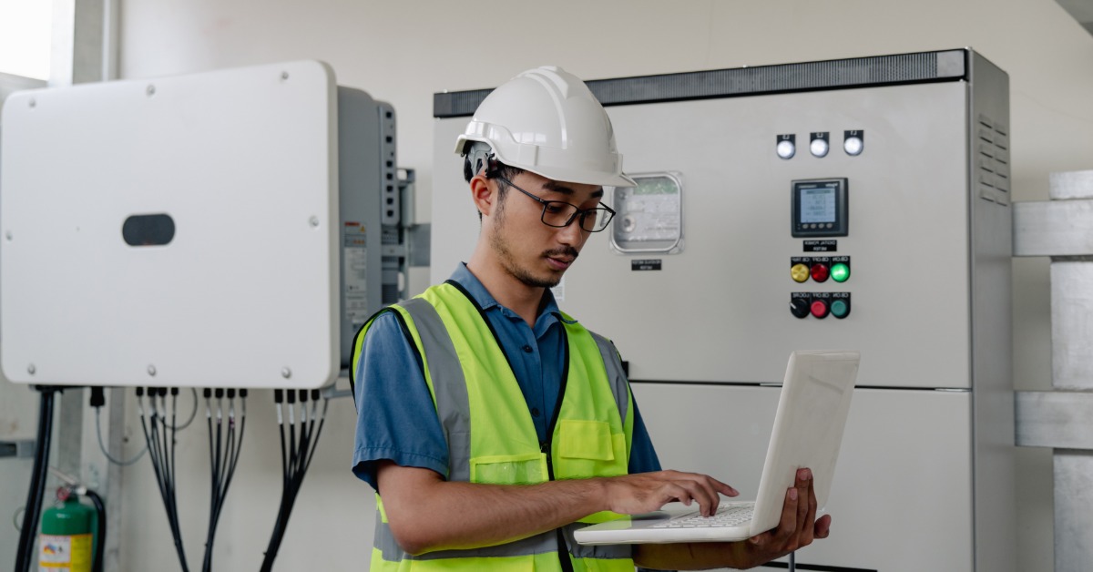 Inverter Efficiency Ratings Explained Efficiently 1 A worker wearing a safety vest and a white helmet, holding a white laptop inside a room with a large energy converter.