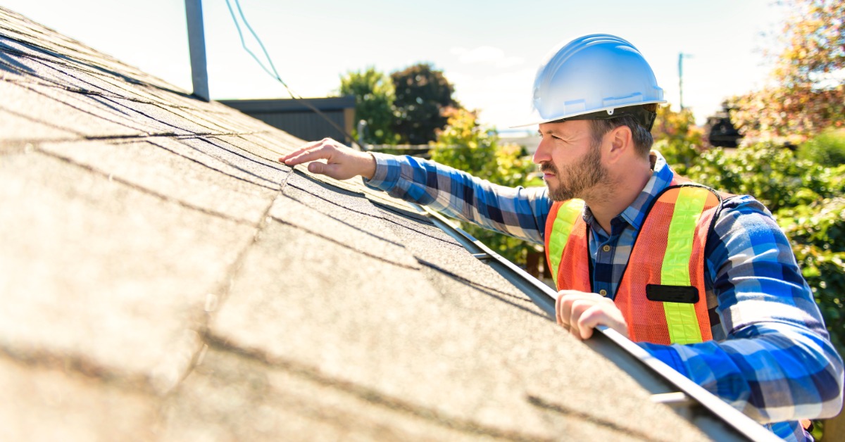 An Overview of Residential Solar Rooftop Assessments 1 A worker wearing a safety vest and a white helmet touching and looking up close at the shingles on a home roof.
