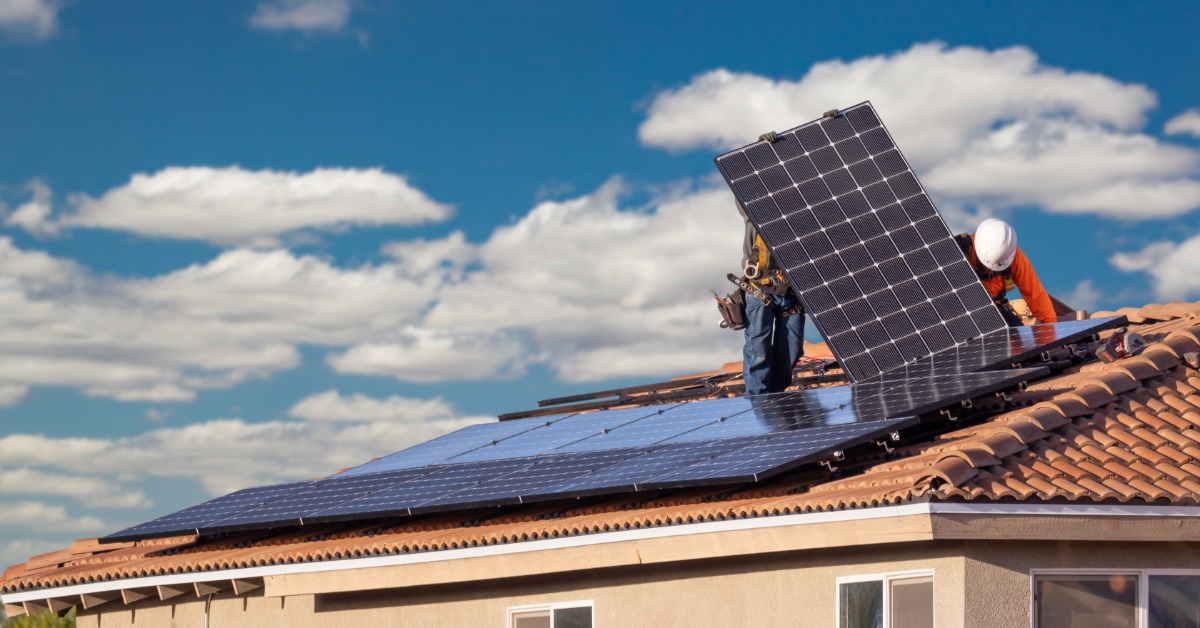 An Overview of Residential Solar Rooftop Assessments 2 Two workers holding a large solar panel upright on the roof of a home, next to multiple rows of panels in place.