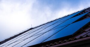 FAQ 6 Multiple rows of solar panels on top of a roof with clay shingles, covered in water drops under a cloudy sky.