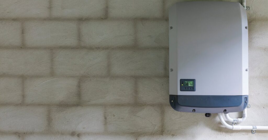 A Look at the Technical Specifications of the Powerwall 3 1 A grey rectangular power storage unit with a small screen in the bottom left, attached to a grey brick wall.