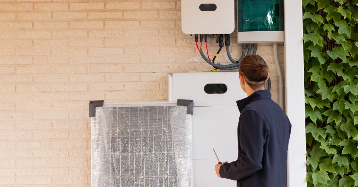 A Look at the Technical Specifications of the Powerwall 3 2 A man standing in front of a small white battery placed on the top part of a beige wall over a large control panel.