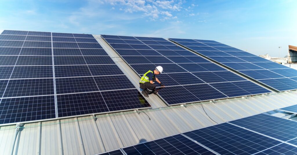 Commercial Solar Interconnection Requirements 1 A worker wearing a safety vest and a helmet fixing a solar panel on the corner of a section with interconnected panels.