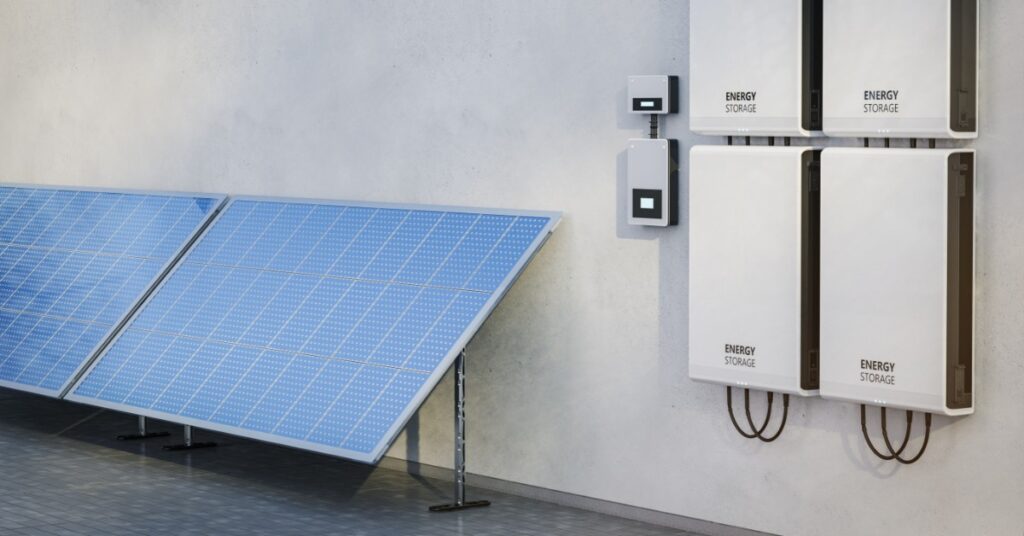 Megapack vs. Powerwall: Core Differences 2 Four white rectangular boxes placed on a wall next to each other, with two large solar panels on the side.