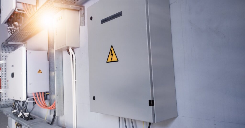 A large gray box with a small lighting sticker in the front and multiple cables attached underneath placed on a wall.