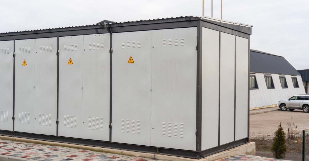 Megapack Installation and Site Requirements 1 A large white box with a tilted top and small electric signs placed on a concrete slab outdoors next to a building.