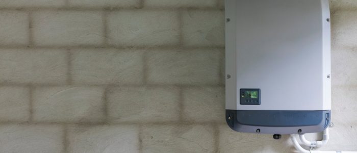 A grey rectangular power storage unit with a small screen in the bottom left, attached to a grey brick wall.