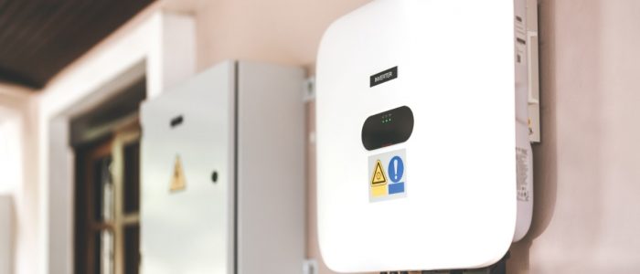 A square box with multiple wires plugged in at the bottom, placed near the top of a wall next to another metal box.