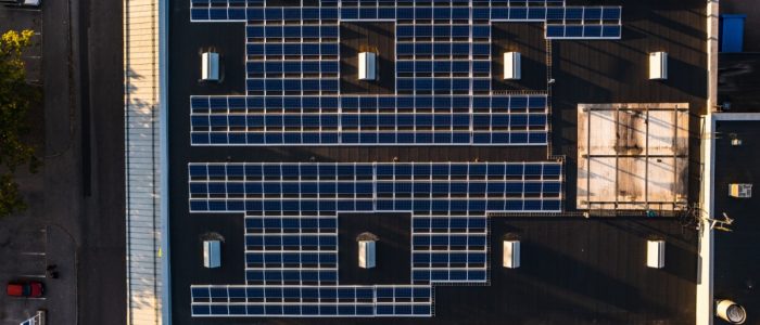 An aerial view of a large building with multiple rows of solar panels on the roof, surrounded by a large parking lot.