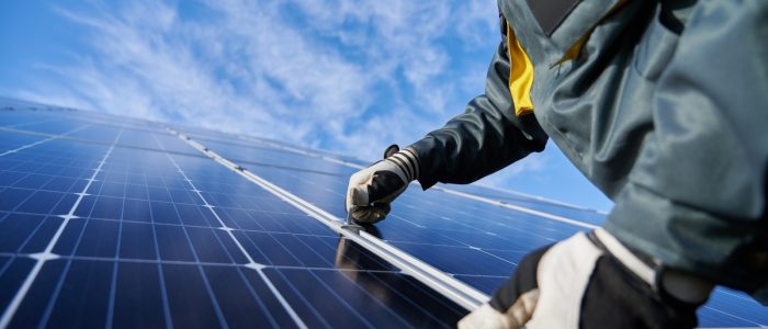 Residential Solar Panels vs. Community Solar Worker wearing protective gloves and a heavy-duty jacket installing a large solar panel on a sunny day.