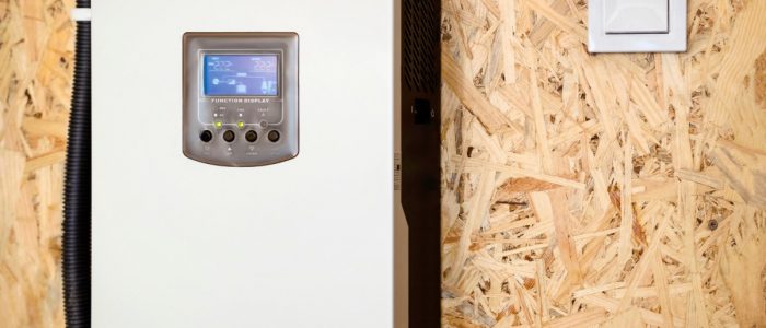 A solar inverter with multiple cables and a small digital screen, mounted on a brown wall between white door frames.