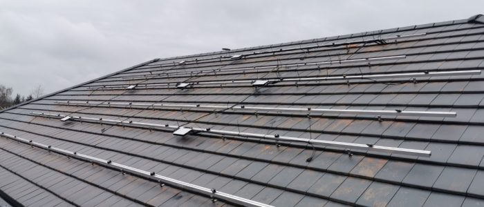 A roof covered in small shingles, with a large metal structure spreading across with small microinverters attached.
