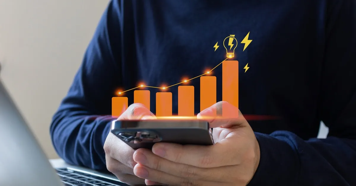 Close-up to the hands of a man holding a smartphone with a digital orange graphic and a lightbulb floating on top.