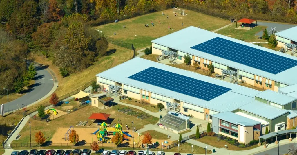 Aerial view of a school with a large parking lot and two buildings, each one with multiple solar panels on the roof.