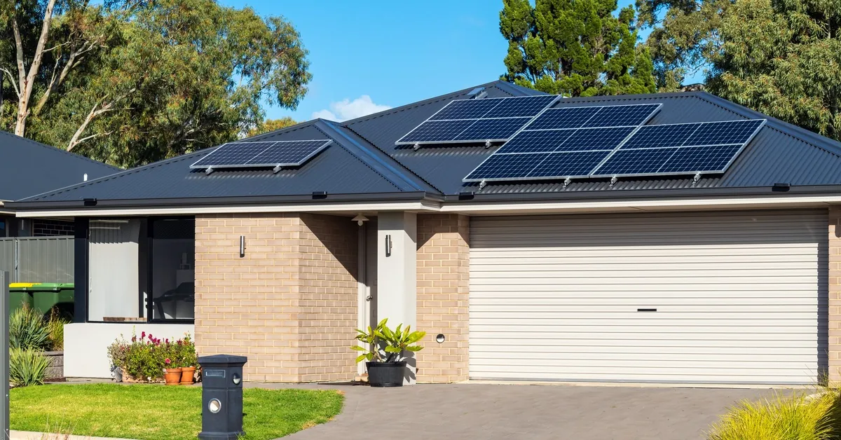 Learn 8 One-story home with a large white garage door, brick walls, and a sloped roof with multiple solar panel units.