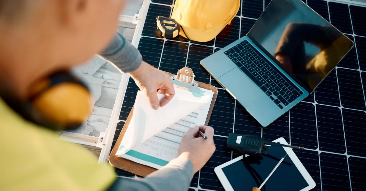 Learn 5 A man writing on a piece of paper attached to a clipboard next to a laptop and a tablet placed on top of a solar panel.