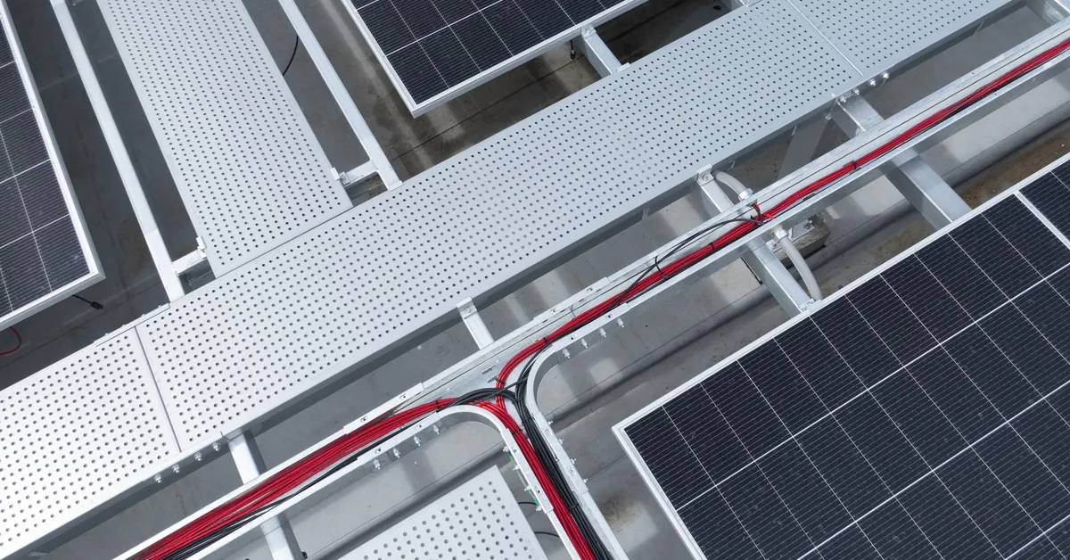 A close-up of the red and black wiring running between large solar panels inside long plastic tubes without a top.