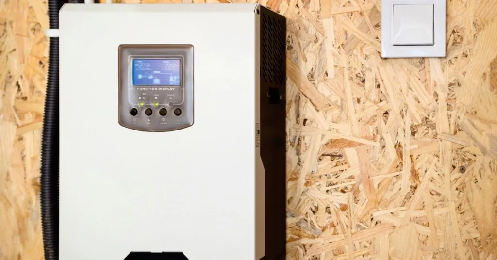 Integrating Tesla Powerwalls With Electrical Systems 3 A solar inverter with multiple cables and a small digital screen, mounted on a brown wall between white door frames.