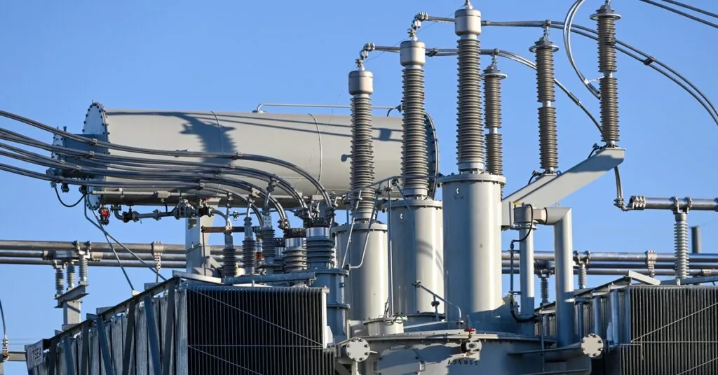 How Tesla Megapack Batteries Stabilize the Electrical Grid 2 A close-up of the top part of an electrical grid with multiple connectors, cables, and coils, on a sunny day.