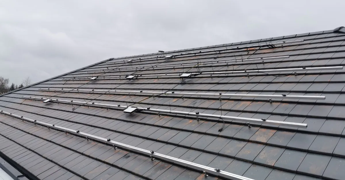 Learn 7 A roof covered in small shingles, with a large metal structure spreading across with small microinverters attached.