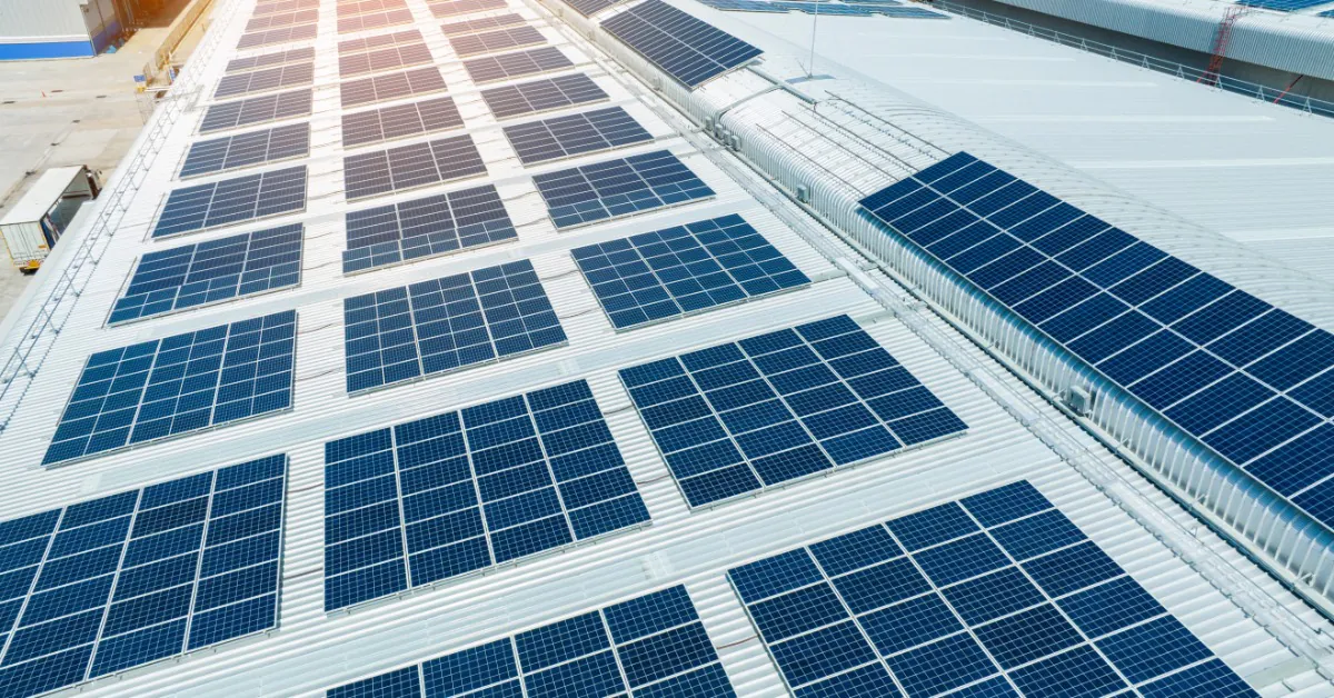 An aerial view of the roof of a large white building covered in multiple rows of solar panels on a sunny day.