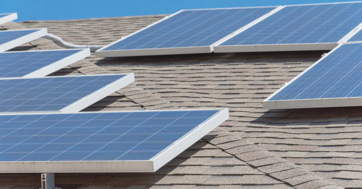How To Do Whole-Home Backup With Tesla Powerwall 1 A close-up of multiple solar panels placed on a tilted roof with asphalt shingles, under the sun with a clear sky.