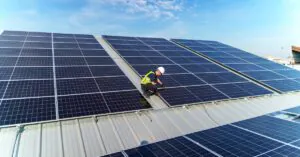FAQ 5 A worker wearing a safety vest and a helmet fixing a solar panel on the corner of a section with interconnected panels.