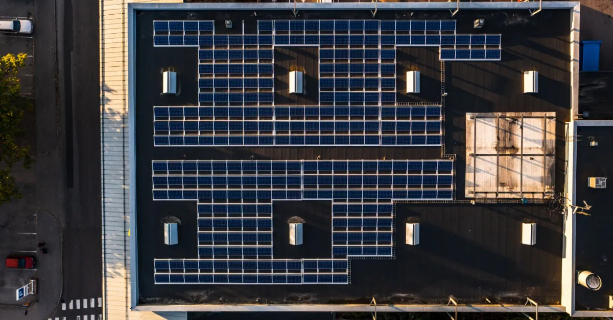 An aerial view of a large building with multiple rows of solar panels on the roof, surrounded by a large parking lot.